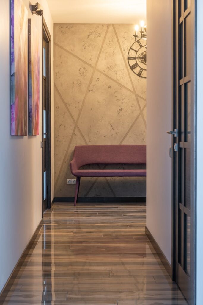Passage interior with textile bench on laminate under shiny lamp against clock on ornamental wall in house